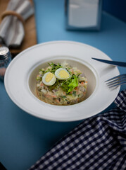 Traditional salad Olivier. Christmas and New year food. White plat with fork and knife on blue background with copy space. Top view, flat lay. Microgreen, quail eggs. Serving at a restaurant.