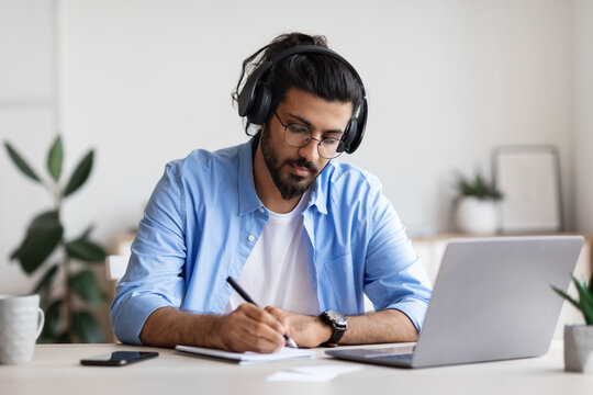 Distance Learning. Young Arab Guy In Headphones Studying With Laptop At Home