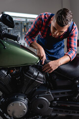 young mechanic pointing with finger while making diagnostics of motorbike in workshop