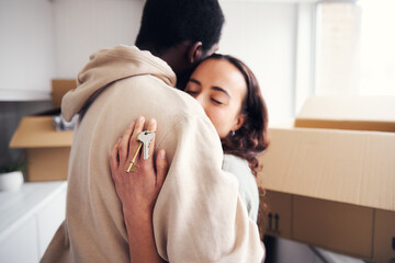 Young Couple With Keys To New Home Hugging As They Unpack Removal Boxes In Kitchen Together
