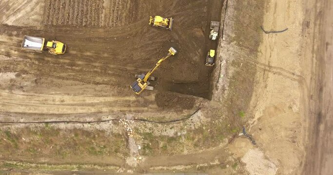 Drone aerial moves over construction site, quarry, vehicles, and tractors as they dig and push soil and dirt for future residential businesses and apartments