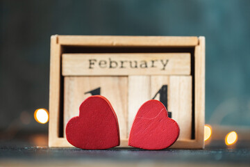 Two red hearts against the wooden calendar of blocks with the date of February 14 on the blurred dark concrete background. two red hearts with bokeh lights behind. Happy Valentine's day.