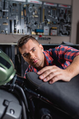 Fototapeta na wymiar young mechanic looking at camera while making diagnostics of motorbike on blurred foreground