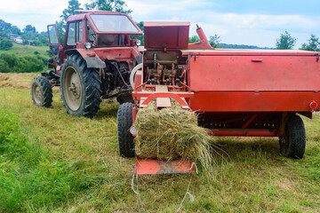 The process of harvesting hay for cattle, a tractor making bales in the field, old machinery.