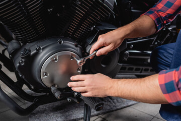 partial view of mechanic unscrewing cap of motorbike gearbox with socket wrench