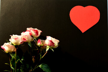 Obraz premium On the black surface of the leaf lies a bouquet of fresh flowers of roses and a red heart in the upper corner. Valentine's day postcard.