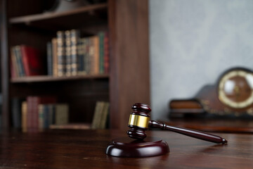 Law theme. Judge chamber. Judge’s gavel on brown desk. Collection of legal books in the bookshelf.