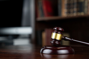 Law theme. Judge chamber. Judge’s gavel on brown desk. Collection of legal books in the bookshelf.