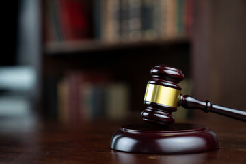 Law theme. Judge chamber. Judge’s gavel on brown desk. Collection of legal books in the bookshelf.