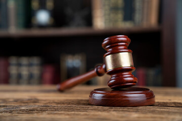 Law theme. Judge chamber. Judge’s gavel on brown desk. Collection of legal books in the bookshelf.