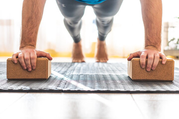closeup of man's hands on yoga blocks doing push-ups at home on an exercise mat, man wears gray leggings