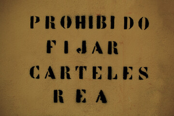 Spanish text forbidding the posting of notices or posters spray painted onto a brown wall