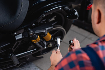 cropped view of mechanic holding socket wrench near motorbike, blurred foreground