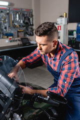 young technician in overalls examining motorcycle in workshop