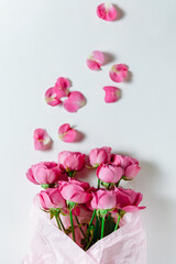 Flower bouquet of pink roses and other mixed flowers wrapped in soft pink paper. The white background is filled with randomly scattered pink petals