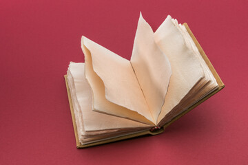 Open antique style book with pages of rough paper with jagged edges, antique leather hardcover notebook  on cardinal red background