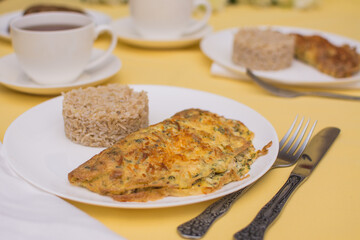 Egg omelet with chicken and cheese. Brizol with brown rice in a white ceramic bowl on a yellow tablecloth.