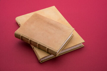 Two antique light brown leather hardcover books, one small on other large on cardinal red color background
