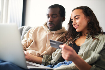 Young Couple At Home Sitting On Sofa Holding Credit Card Using Laptop To Shop Online