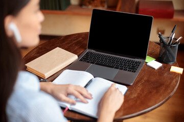 Woman sitting at desk using laptop with blank screen, mockup