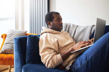 Young Man Relaxing At Home Lying On Sofa Using Laptop To Work From Home Or Shop Online