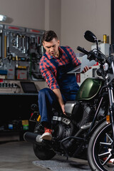Fototapeta na wymiar repairman in overalls checking motorcycle while holding laptop