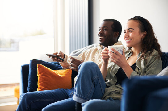 Smiling Young Couple Relaxing At Home Sitting On Sofa Watching On Demand TV Together