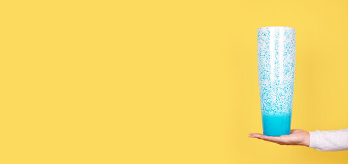 Hand with turquoise glass vase on yellow background.