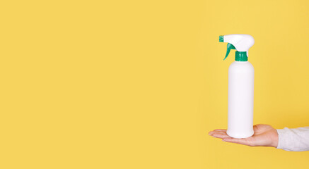 Hand with antiseptic in white spray bottle on yellow background.