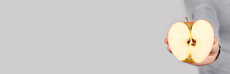 Hand with half apple on grey background.