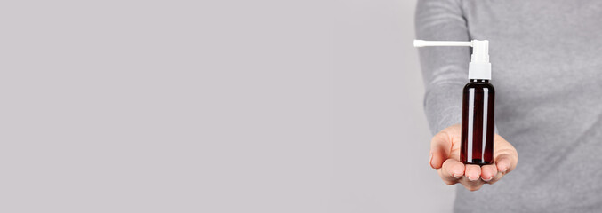 Hand with medical throat spray on grey background.