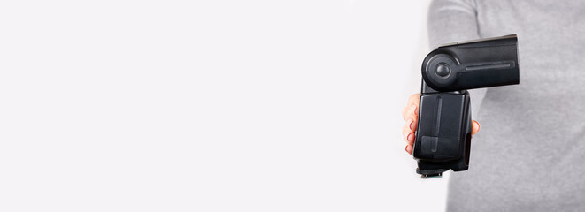 Hand with black camera flash on grey background.