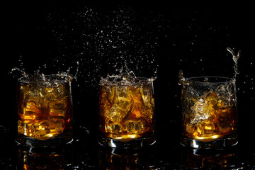 set of three glasses of scotch whiskey with splash and ice on black background