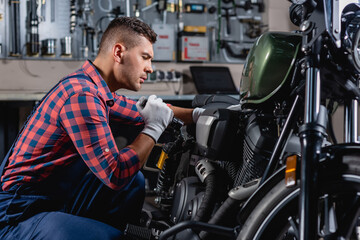 mechanic in overalls using flashlight during diagnostics of motorcycle