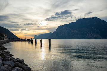 Scenic sunset on Lake Garda near Malcesine, Italy. Sailboats are anchored to a pier, clouds in the orange sky.