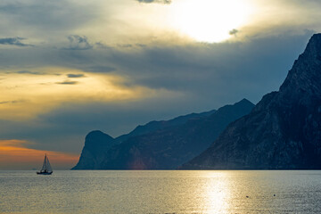 Scenic sunset on Lake Garda near Malcesine, Italy. A sailboat is sailing on the lake, dramatic clouds in the orange sky