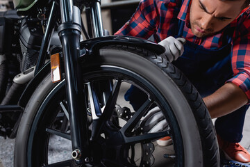 Plakat young mechanic checking wheel of motorcycle in workshop