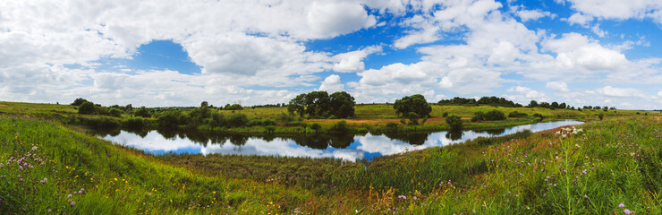 Beautiful panoramic rural landscape with calm river and green hills with trees at summer day.
