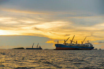 Obraz premium Large cargo ship for logistic import export goods anchor at sea in evening with golden sunset