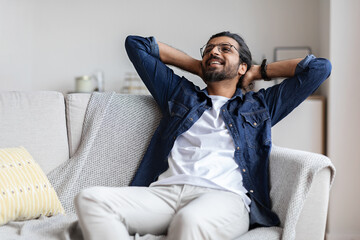 Relaxed smiling arab guy leaning back on couch, relaxing at home