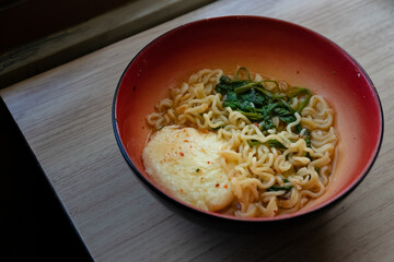 a bowl of instant noodles with eggs and vegetables by the window