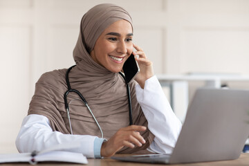 Cheerful muslim lady doctor having conversation on phone with patient