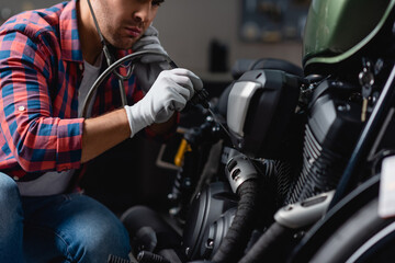 Fototapeta na wymiar cropped view of young repairman examining motorbike engine with stethoscope