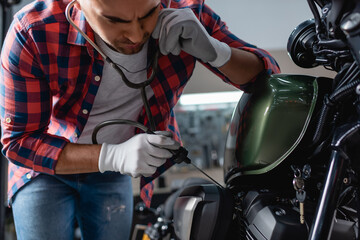 young mechanic in gloves checking motorbike engine with stethoscope