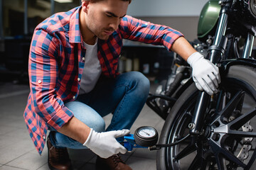 young mechanic in plaid shirt measuring air pressure in tire of motorcycle with manometer