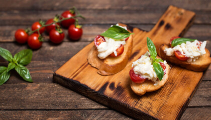 Bruschettas with stracciatella cheese cherry tomatoes and basil on wooden cutting board. Selective focus.