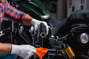 cropped view of mechanic pouring engine oil into funnel near motorbike on blurred background
