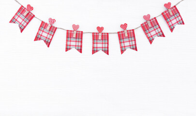 Cute checkered fabric flags attached to jute rope with clothespins with hearts on white wooden background for valentine's day greeting banner. Red rectangular flags isolated on white background.