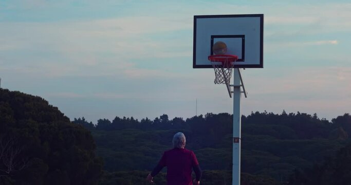 Senior man dunking basketball through hoop on outdoors court