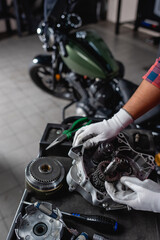 Fototapeta na wymiar cropped view of mechanic near disassembled gearbox and motorbike on blurred background